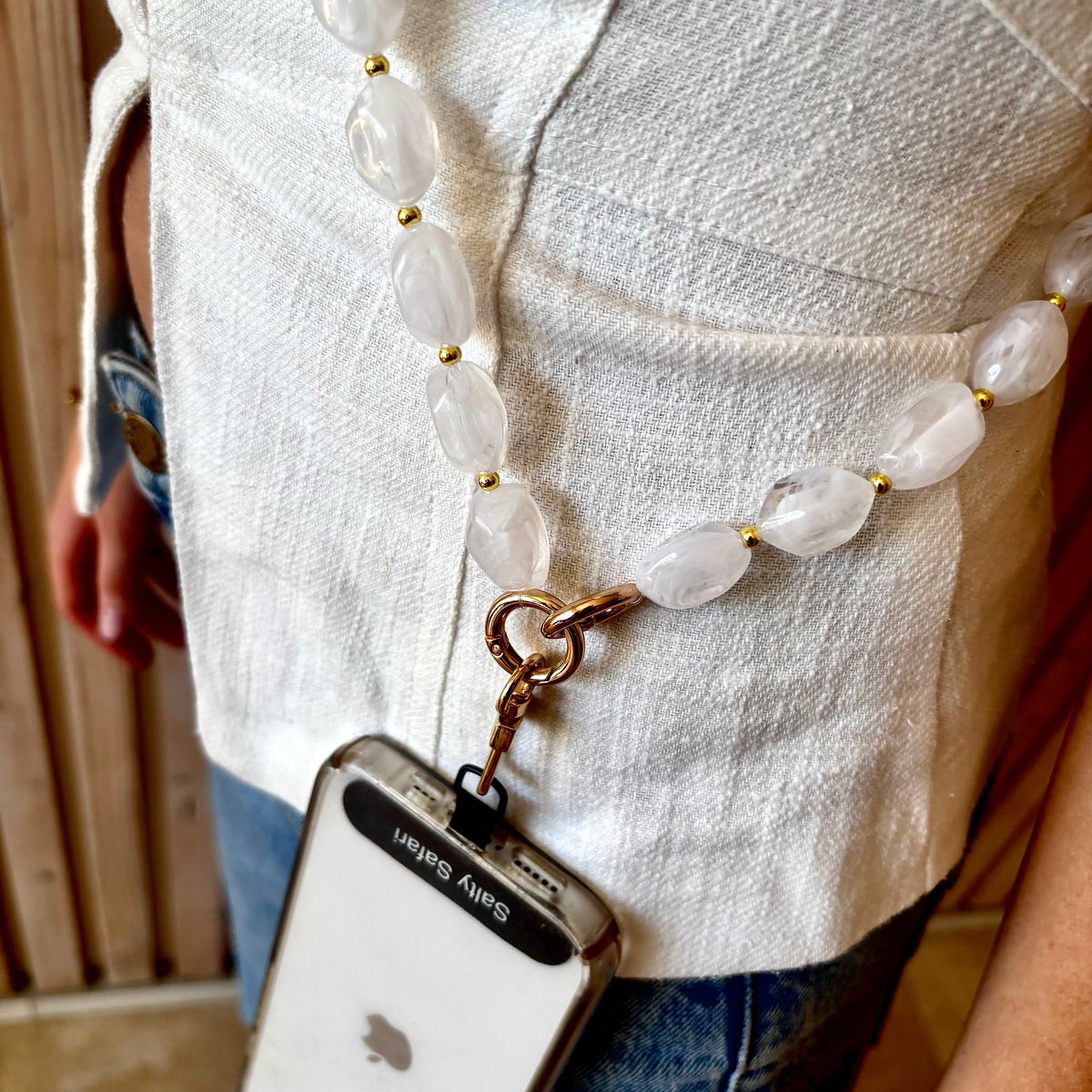 Person wearing a beaded necklace with a phone holder attached, standing indoors.