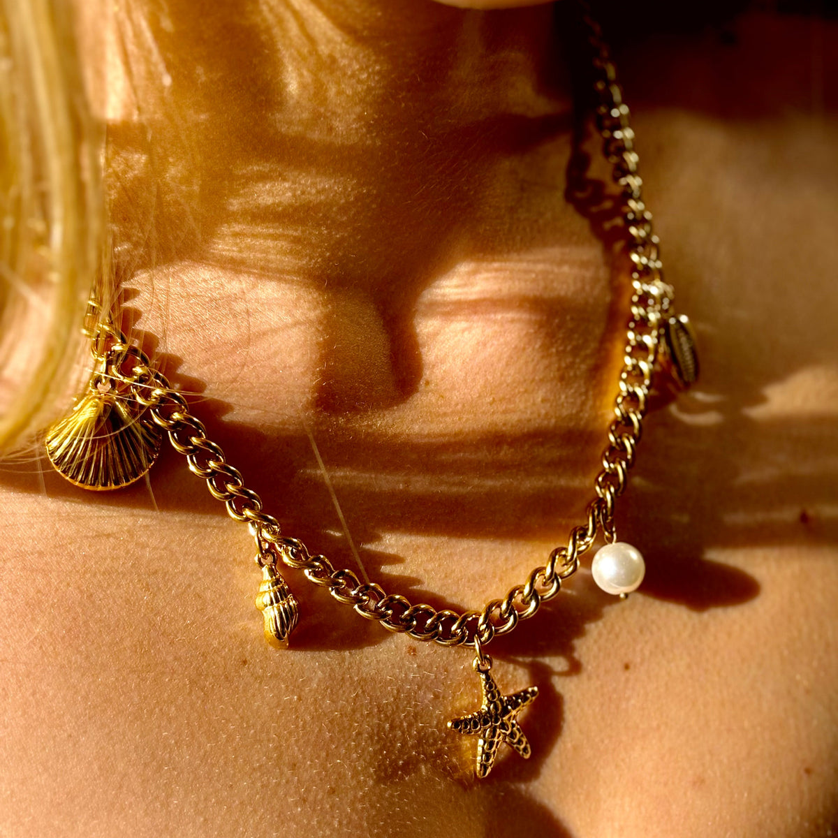 Necklace with starfish and shell charms on a person's neck, sunlit background